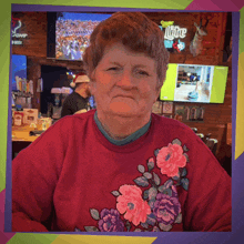 a woman wearing a red sweater with flowers on it sits in front of a miller lite sign