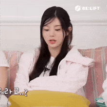 a girl in a pink jacket sits on a couch with be lift written on the bottom right