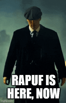 a man in a suit and hat is standing in front of a sign that says rapuf is here now .