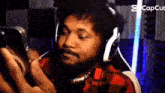 a man with a beard is wearing headphones and looking at a cell phone .