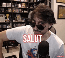 a man wearing sunglasses and a shirt that says salut stands in front of a microphone