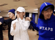 a man wearing a blue wtaps hoodie stands next to two other men