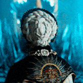 a woman with a braided hairstyle is wearing a black and gold embroidered cape