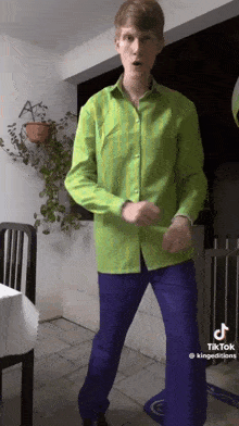 a man in a green shirt and purple pants is dancing in a room .