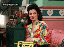 a woman in a colorful jacket is sitting on a couch and talking to someone .