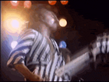 a man in a striped shirt is playing a bass guitar on stage .