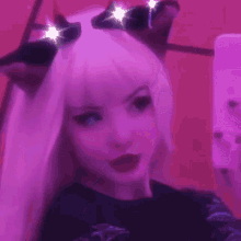 a girl wearing a cat ear headband is taking a selfie with her cell phone .
