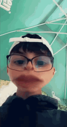 a young boy wearing glasses and a white hat makes a funny face .
