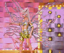 a woman in a gold and silver costume with wings is standing in front of a pink wall