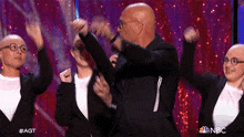 a group of bald people are dancing on a stage with their arms in the air .
