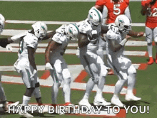 a group of football players are dancing on a field while holding a football .