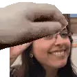 a woman wearing glasses is smiling and a hand is reaching out to touch her face .