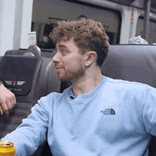 a man wearing a light blue the north face sweatshirt sits on a bus