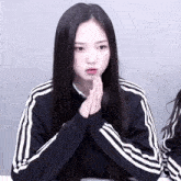 a girl with long black hair wearing a black adidas jacket