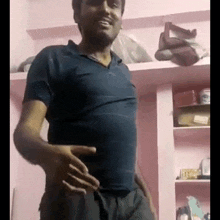 a man in a blue shirt is standing in a room with his hands on his hips and smiling .
