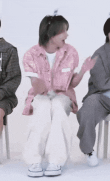 a man in a pink shirt and white pants is sitting on a chair with his feet crossed .