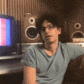 a man wearing glasses sits on a couch in front of speakers