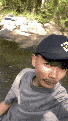 a man wearing a gray shirt and a black hat with the letter f on it is taking a selfie