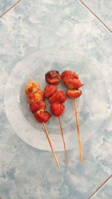 three skewers of food on a clear plate on a tiled floor