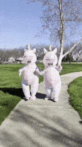 two people dressed in unicorn costumes holding hands on a sidewalk