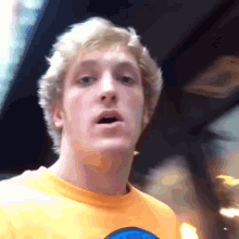 a man wearing a yellow t-shirt with a blue circle on it looks at the camera