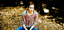 a woman sits on a pile of leaves in a forest