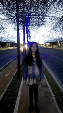 a girl is standing on a sidewalk in front of a purple light