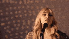 a woman is singing into a microphone and dancing in front of a wall with polka dots .