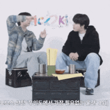 two men are sitting at a table and one of them is pointing at something