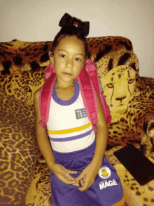 a little girl is sitting on a leopard print couch with a bag on her back