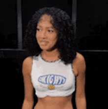 a young woman with curly hair is wearing a white crop top with the word mighty on it .