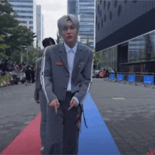 a man in a grey suit is walking on a red carpet