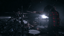 a man in a plaid shirt is playing a drum set