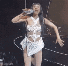 a woman in a white dress is singing into a microphone while dancing on stage .