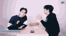 two men sitting at a table with confetti falling around them .