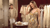 a woman in a floral dress stands in front of a man in a beige jacket
