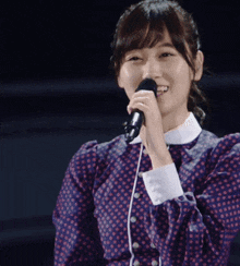 a woman in a purple polka dot dress singing into a microphone