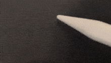 a close up of a white pencil pointing to a black surface .