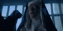 a nun wearing glasses and a blue robe is standing in a dark room .