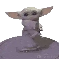a baby yoda statue is sitting on top of a purple sphere .