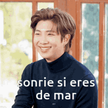 a man wearing a black turtleneck sweater smiles with the words sonrie si eres de mar written below him