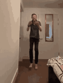 a man is jumping in the air in a room with a bed and a mirror