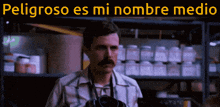 a man with a mustache is standing in front of a shelf with the words peligroso es mi nombre medio above him