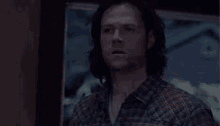 a man with long hair is standing in front of a painting on the wall .