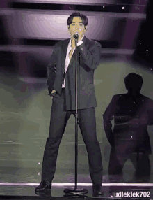 a man in a suit is singing into a microphone with judleklek702 written below him