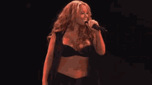 a woman is singing into a microphone on a stage in a crop top .
