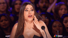 a woman with a surprised look on her face stands in front of a microphone with the nbc logo in the background