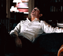 a man in a white shirt is sitting on a couch with his arms outstretched