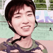 a young man wearing a helmet and a camouflage shirt is smiling for the camera .