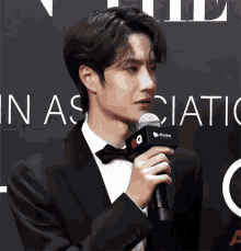 a man in a tuxedo is holding a microphone in front of a sign that says ' in association '